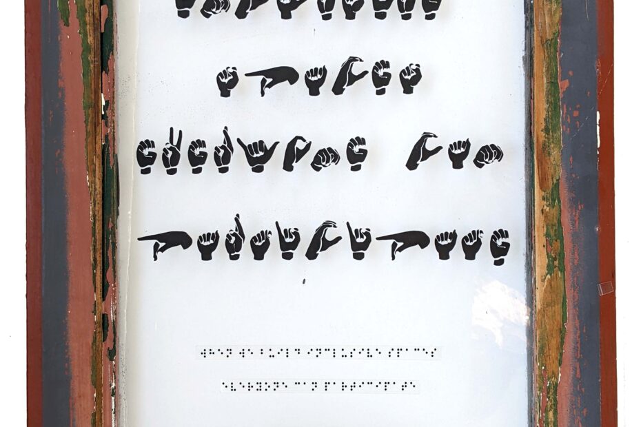 artwork on a glass window with sign language fingerspelling and braille meant to communicate a message hearing and seeing people can't access.